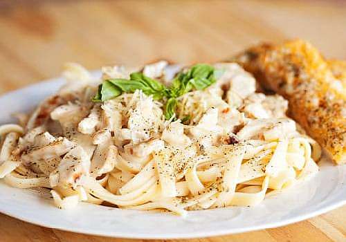 A white plate with pasta and chicken on it.
