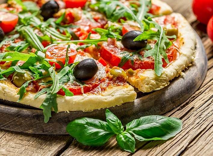 A pizza with tomatoes and olives on a wooden table.