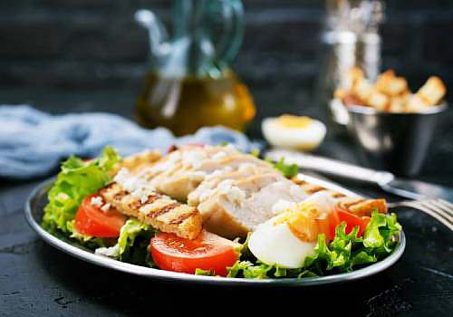 A plate of chicken salad with tomatoes and eggs.
